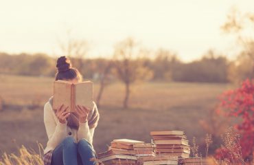 Women sitting on books reading in a field with Fall leaves and trees